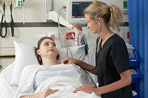 A female doctor uses a stethoscope to listen to the heartbeat of a female patient laying in a hospital bed