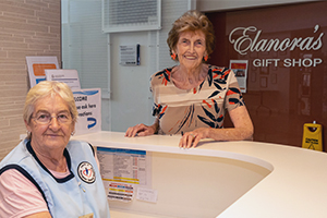 One woman sits a a counter while another stands beside her. Behind the standing woman a sign reads Elanora's gift shop