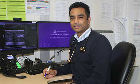 Dr Indunil Weerasena sits in front of two computer screens. Medical images are on one of the screens.
