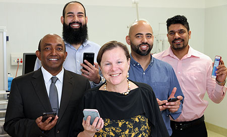 Four men and a woman standing in a treatment room. Each person is holding a mobile phone.